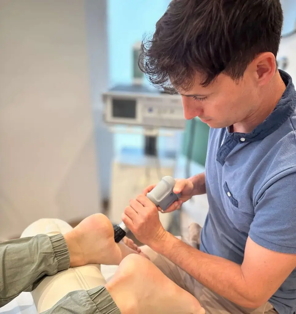 Physiotherapeut wendet eine Stoßwellentherapie am Fuß eines Patienten an